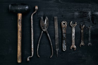 Siyah ahşap masanın üzerinde yatan eski, paslı araçları. Çekiç, keski, metal makas, İngiliz anahtarı.