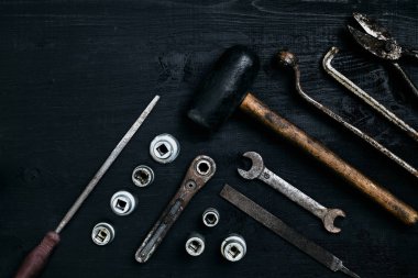 Siyah ahşap masanın üzerinde yatan eski, paslı araçları. Çekiç, keski, metal makas, İngiliz anahtarı.