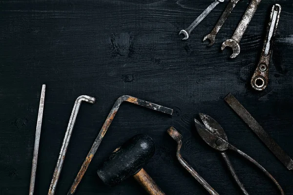 Old, rusty tools lying on a black wooden table. Hammer, chisel, metal scissors, wrench.