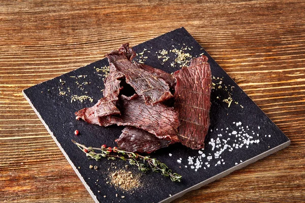 Carne seca picada cortada en tiras en el tablero negro sobre fondo de madera — Foto de Stock