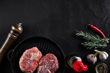 Taze çiğ et. Dana bonfile ve iki mermer sığır biftek ızgara tava ve kızartma yönetim kurulu ile baharat, siyah arka plan Üstten Görünüm.