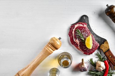 Otlar, sarımsak, zeytinyağı, karabiber, tuz, biberiye ile taze çiğ biftek ve beyaz arka plan üzerinde bir mutfak balta. Üstten Görünüm.