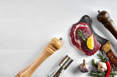 Otlar, sarımsak, zeytinyağı, karabiber, tuz, biberiye ile taze çiğ biftek ve beyaz arka plan üzerinde bir mutfak balta. Üstten Görünüm.