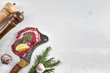 Otlar, sarımsak, zeytinyağı, karabiber, tuz, biberiye ile taze çiğ biftek ve beyaz arka plan üzerinde bir mutfak balta. Üstten Görünüm.