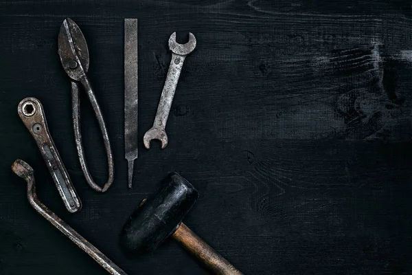 Herramientas viejas y oxidadas sobre una mesa de madera negra. Martillo, cincel, tijeras de metal, llave inglesa . — Foto de Stock