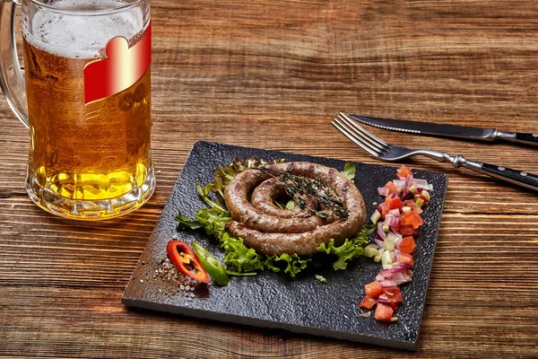 Hausgemachte Wurst mit Knoblauch und Gewürzen auf einem Schieferteller, ein Glas Bier hinter dem Teller auf einem Holztisch — Stockfoto