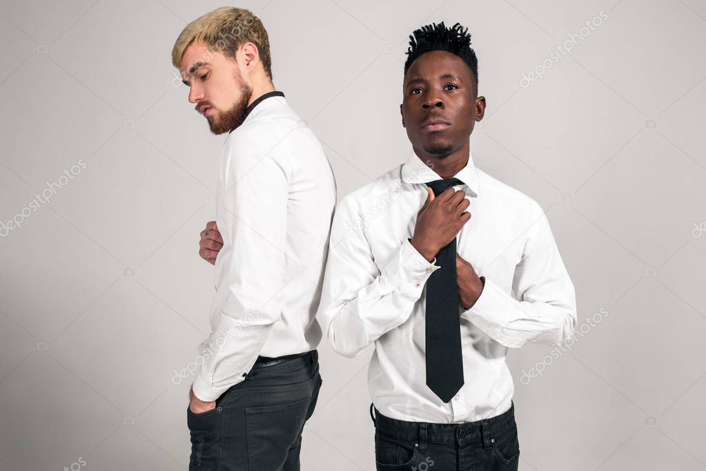Friends. Two guys in white shirts and dark pants posing in the studio on a white background