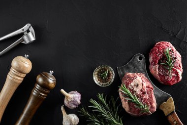 Tuz, biber, biberiye, sarımsak ve siyah arka plan üzerine bir balta ile iki ham taze antrikot biftek