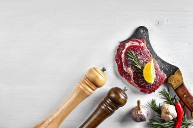 Otlar, sarımsak, zeytinyağı, karabiber, tuz, biberiye ile taze çiğ biftek ve beyaz arka plan üzerinde bir mutfak balta. Üstten Görünüm.