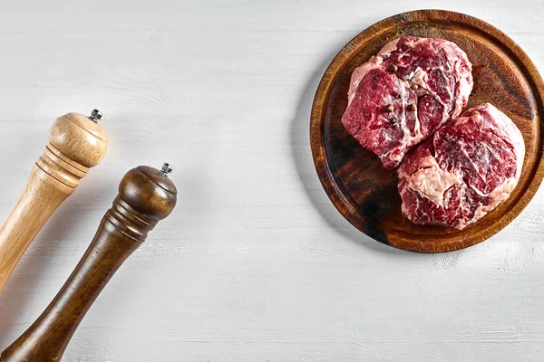 Filete de res crudo con especias e ingredientes para cocinar sobre tabla de cortar de madera y fondo blanco . — Foto de Stock