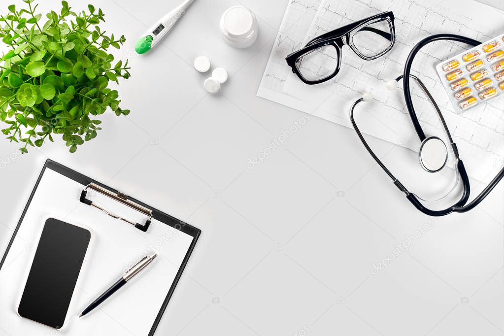 Stethoscope in the office of doctors.Top view of doctors desk table, blank paper on clipboard with pen. Copy space. Designers blank