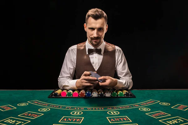 Schöner Dealer, der Spielkarten und Chips auf grünem Tisch mischt — Stockfoto
