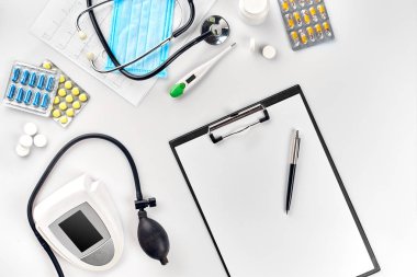 Stetoskop, çok renkli hapları, maske ve beyaz masada termometre ile beyaz elektrik tonometer. Üstten Görünüm