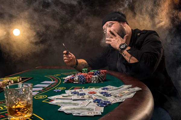 Γενειοφόρος άνδρας με πούρο και γυαλί που κάθεται στο τραπέζι του πόκερ σε ένα καζίνο. Τα τυχερά παιχνίδια, παίζουν χαρτιά και ρουλέτα. — Φωτογραφία Αρχείου