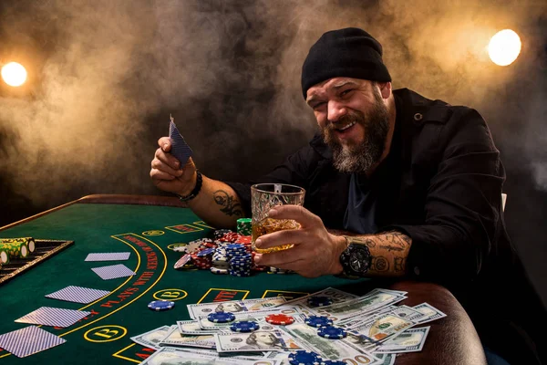 Skäggig man med cigarr och glas som sitter vid pokerbordet i ett kasino. Hasardspel, spelkort och roulette. — Stockfoto