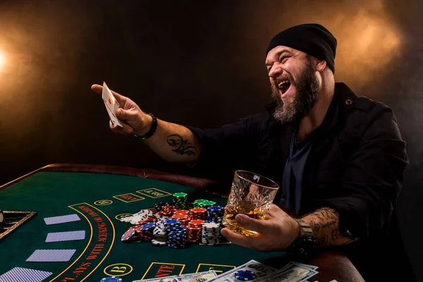 Skäggig man med cigarr och glas som sitter vid pokerbordet i ett kasino. Hasardspel, spelkort och roulette. — Stockfoto