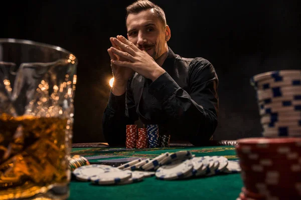 Joven hombre guapo sentado detrás de la mesa de póquer con cartas y fichas — Foto de Stock