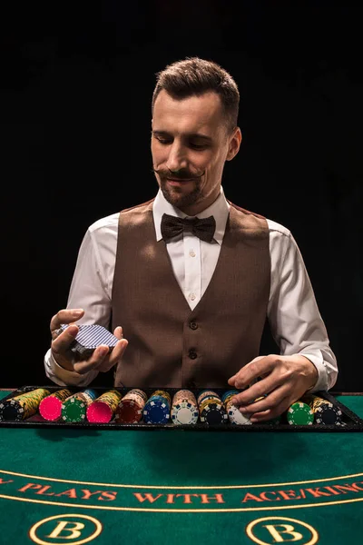 Das Porträt eines Croupier hält Spielkarten und Spielchips auf dem Tisch. schwarzer Hintergrund — Stockfoto