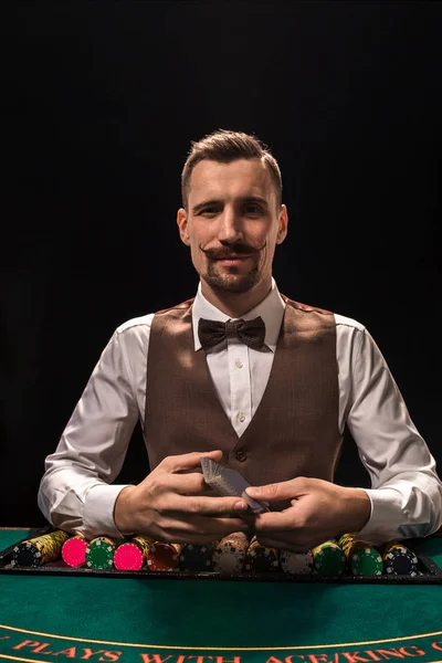 Retrato de un croupier es la celebración de cartas, fichas de juego en la mesa. Fondo negro — Foto de Stock