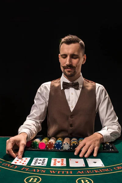 Das Porträt eines Croupier hält Spielkarten und Spielchips auf dem Tisch. schwarzer Hintergrund — Stockfoto