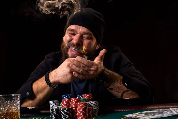 Бородатий чоловік з сигарою і склом сидить за покерним столом в казино. Азартні ігри, гральні карти та рулетка . — стокове фото