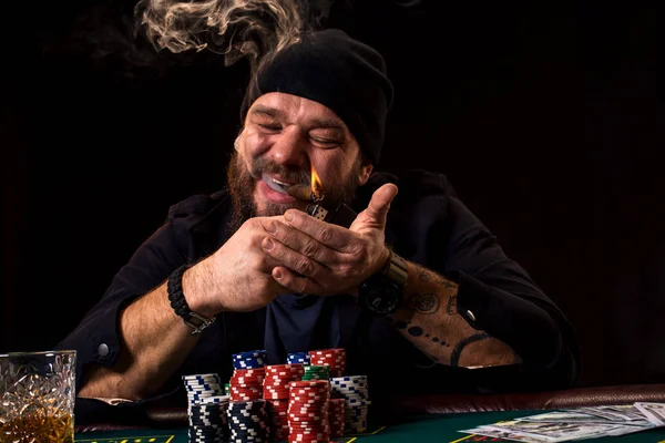 Skäggig man med cigarr och glas som sitter vid pokerbordet i ett kasino. Hasardspel, spelkort och roulette. — Stockfoto