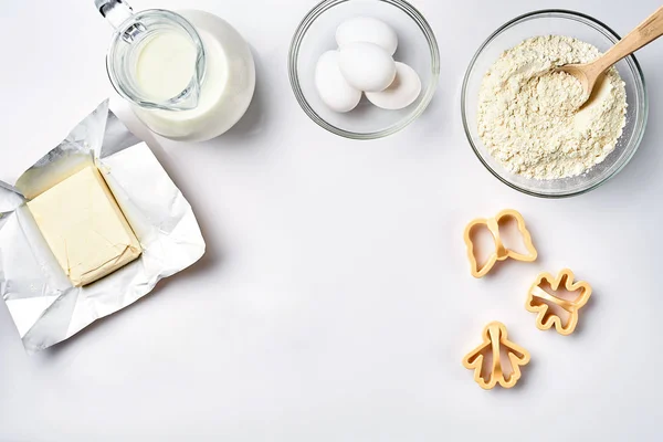 Objekt och ingredienser för bakning, plast formar för cookies på en vit bakgrund. Mjöl, ägg, mjölk, smör, grädde. Ovanifrån, utrymme för text — Stockfoto