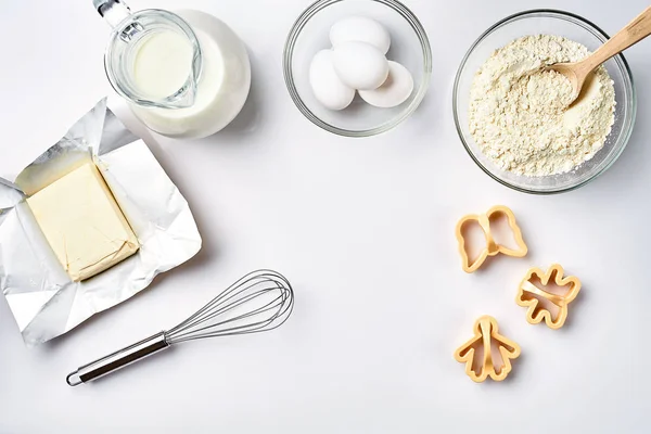 Objetos e ingredientes para assar, moldes de plástico para biscoitos em um fundo branco. Farinha, ovos, batedor, leite, manteiga, creme. Vista superior, espaço para texto — Fotografia de Stock