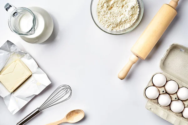 Предмети та інгредієнти для випічки, пластикові форми для печива на білому тлі. Борошно, яйця, шпилька, віночок, молоко, масло, вершки. Вид зверху, простір для тексту — стокове фото