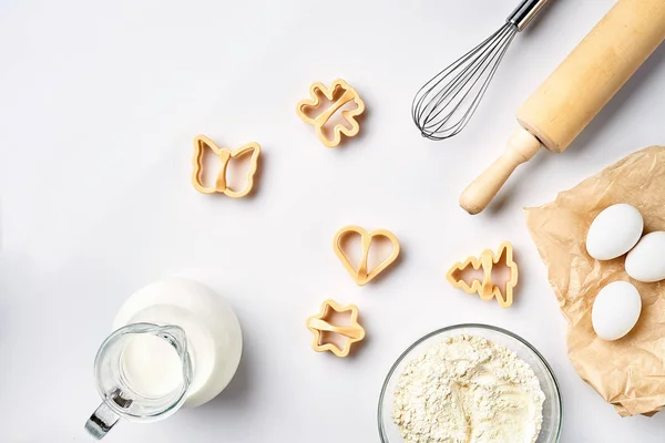 Objetos e ingredientes para assar, moldes de plástico para biscoitos em um fundo branco. Farinha, ovos, rolo, batedor, leite, manteiga, creme. Vista superior, espaço para texto — Fotografia de Stock