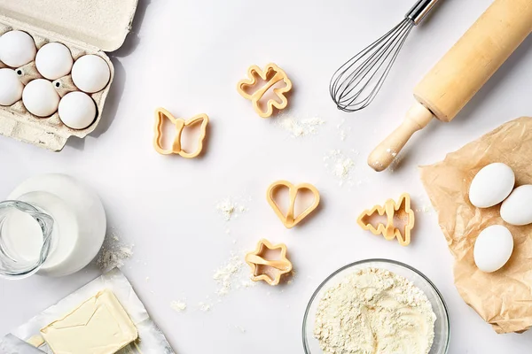 Objetos e ingredientes para assar, moldes de plástico para biscoitos em um fundo branco. Farinha, ovos, rolo, batedor, leite, manteiga, creme. Vista superior, espaço para texto — Fotografia de Stock