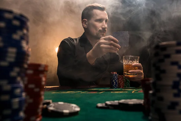 Mladý pohledný muž sedící za pokerový stůl s čipy a karty — Stock fotografie