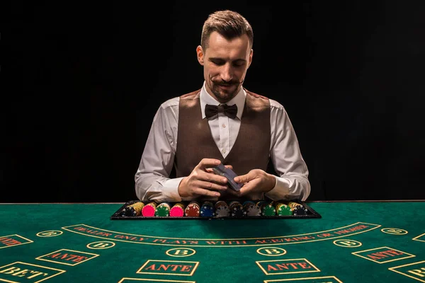 Portrait of a croupier is holding playing cards, gambling chips on table. Black background