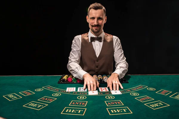 Das Porträt eines Croupier hält Spielkarten und Spielchips auf dem Tisch. schwarzer Hintergrund — Stockfoto