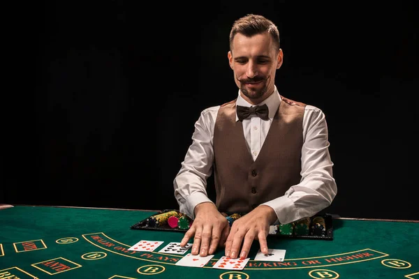 Retrato de un croupier es la celebración de cartas, fichas de juego en la mesa. Fondo negro — Foto de Stock