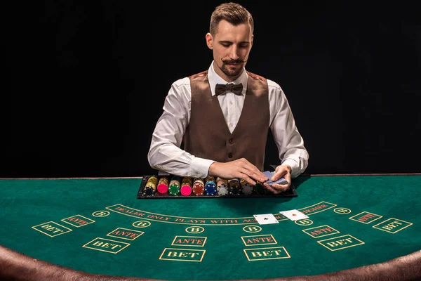 Portrait d'un croupier tient des cartes à jouer, des jetons de jeu sur la table. Fond noir — Photo