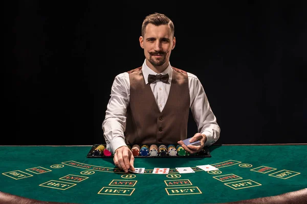 Portrait d'un croupier tient des cartes à jouer, des jetons de jeu sur la table. Fond noir — Photo