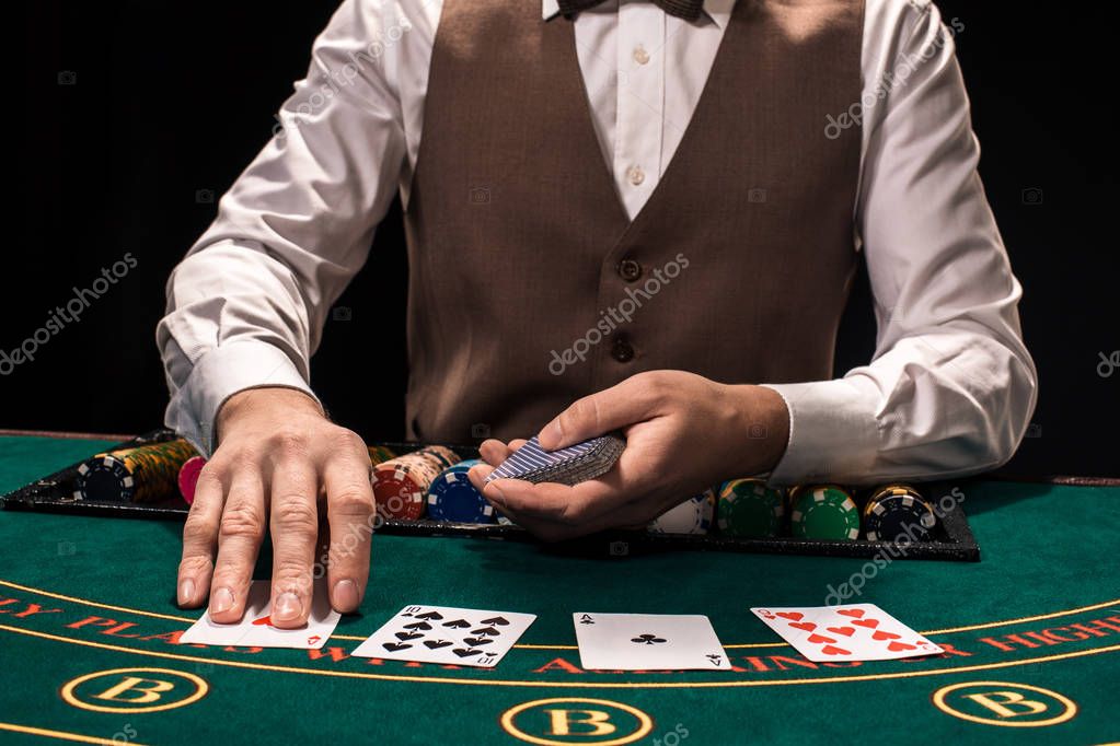 Casino, gambling, poker, people and entertainment concept - close up of holdem dealer with playing cards and chips on green table