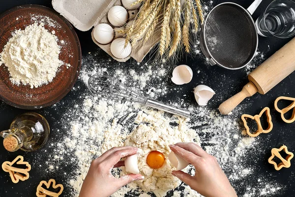 Woman smashes an egg using knife while kneading a pastry. Studio shot. Top view