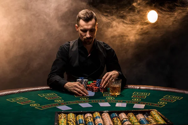 El hombre está jugando al póquer con un cigarro y un whisky. Un hombre ganando todas las fichas en la mesa con humo de cigarrillo grueso . — Foto de Stock