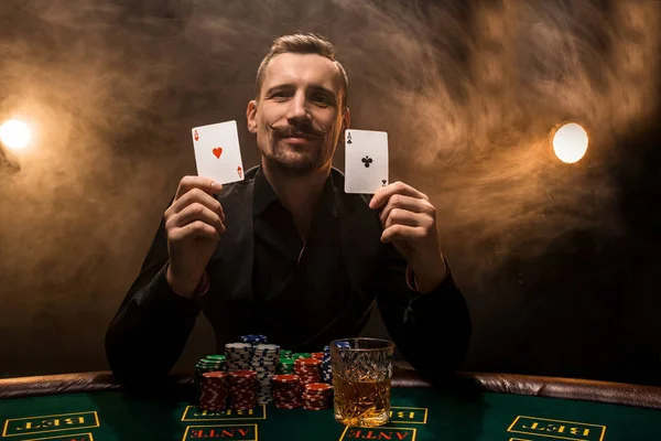 El hombre está jugando al póquer con un cigarro y un whisky, un hombre muestra dos cartas en la mano, ganando todas las fichas en la mesa con humo de cigarrillo grueso . — Foto de Stock