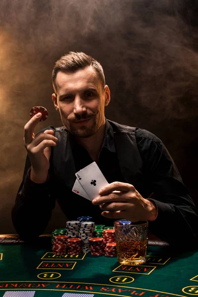 Man is playing poker with a cigar and a whiskey, a man show two cards in the hand, winning all the chips on the table with thick cigarette smoke.