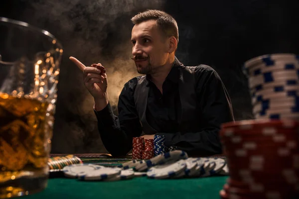 El hombre está jugando al póquer con un cigarro y un whisky. Un hombre ganando todas las fichas en la mesa con humo de cigarrillo grueso . — Foto de Stock