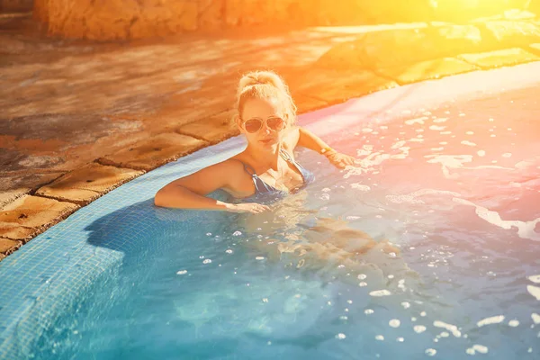 Mujer en traje de baño azul y gafas de sol relajante en la piscina al aire libre con agua turquesa transparente limpia. Bengala solar —  Fotos de Stock