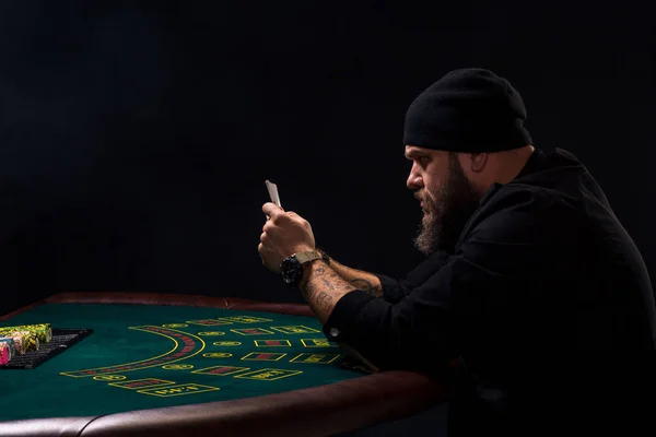 Allvarlig skäggig man sitter vid pokerbordet och hålla kort isolerade på svart. Kopiera utrymme — Stockfoto