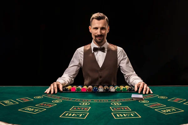 Das Porträt eines Croupier hält Spielkarten und Spielchips auf dem Tisch. schwarzer Hintergrund — Stockfoto