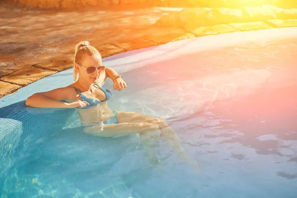 穿着蓝色泳装和太阳镜的妇女在室外泳池里放松, 干净透明的绿松石水。太阳耀斑 — 图库照片