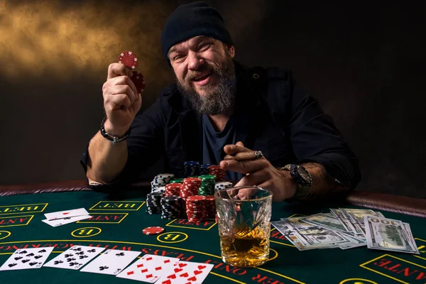 Skäggig man med cigarr och glas som sitter vid pokerbordet i ett kasino. Hasardspel, spelkort och roulette. — Stockfoto