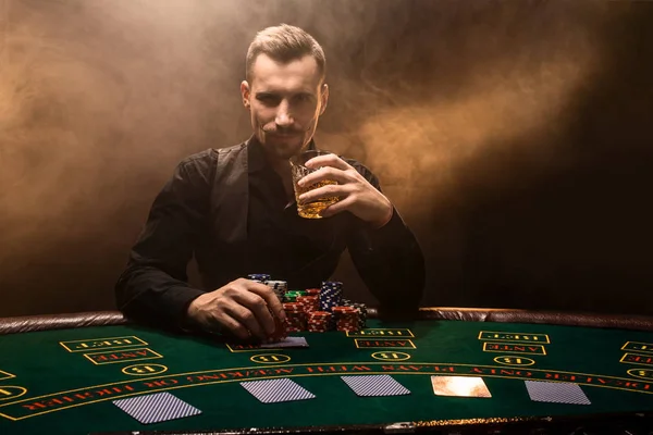 Un joven con un traje de negocios sentado en la mesa de póquer. El hombre juega. El jugador en la mesa de juego jugando a las cartas . — Foto de Stock