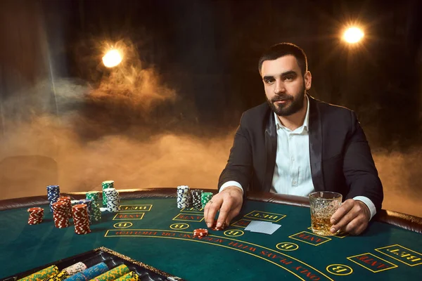 Ein junger Mann im Business-Anzug sitzt am Pokertisch. Der Mensch zockt. der Spieler am Spieltisch, der Karten spielt. — Stockfoto